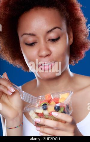 Giovane donna nera che mangia una sana insalata di frutta fresca in un concetto di buona nutrizione e dieta Foto Stock