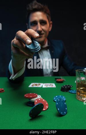 Giocatore di poker gettando chip sul tavolo verde nel casinò. Foto Stock