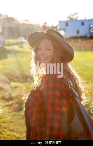 una donna dai capelli rossi splendida che indossa un cappello e un plaid vi guarda indietro nel sole splendente Foto Stock