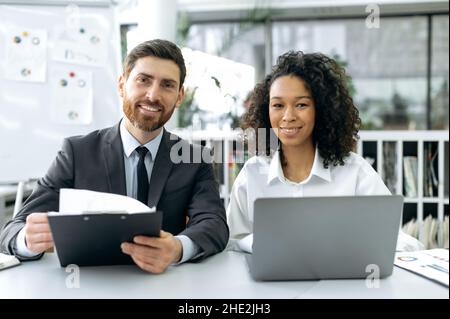 Uomini d'affari multietnici di successo. Fiducioso successo caucasico capo della società, african american donna top manager, stanno guardando la macchina fotografica, sorriso amichevole, seduto in ufficio moderno Foto Stock