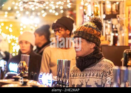 I clienti sono serviti in un bar nei mercatini all'aperto di Natale, Piccadilly Gardens, Manchester, Inghilterra, Regno Unito. Concentrarsi sul primo barista Foto Stock