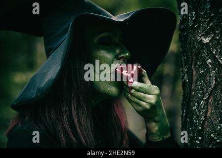 Primo piano di una bella giovane strega con Halloween fare mangiare in giardino Foto Stock