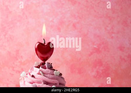 Candela a forma di cuore che brucia sulla crema di cupcake, concetto di giorno di San Valentino, primo piano. Foto Stock