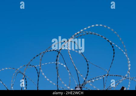 Filo spinato su recinzione con cielo blu Foto Stock