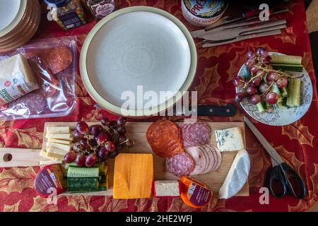 Guardando giù ad un tavolo della sala da pranzo posato con una selezione di formaggi con fette di salsiccia spagnola e tedesca su un asse di legno per pranzo. Foto Stock