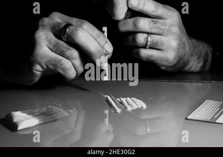 Quest'uomo sta russando la polvere di cocaina con la banconota laminata. Concetto di narcotici. Versione in bianco e nero. Foto Stock