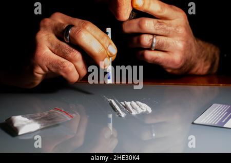 Quest'uomo sta russando la polvere di cocaina con la banconota laminata. Concetto di narcotici. Foto Stock