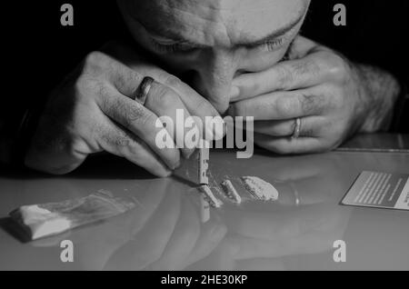 Quest'uomo sta russando la polvere di cocaina con la banconota laminata. Concetto di narcotici. Versione in bianco e nero. Foto Stock
