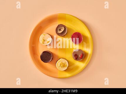 Dolci vegani crudi al mirtillo, lampone, limone, goji e banana su un piatto su sfondo arancione Foto Stock