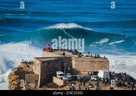 Surfista che cavalca un'onda enorme vicino al faro di Sao Miguel Arcanjo a Nazare, Portogallo. Nazare è noto per avere le onde più grandi in t Foto Stock