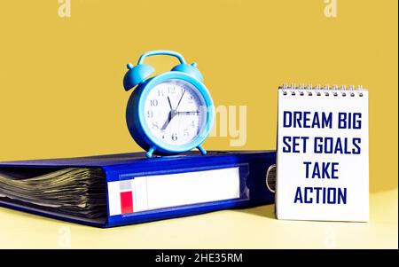 Dream Big - Imposta obiettivi - prendere azione, scrittura a mano in notebook con cartella e orologio su sfondo giallo Foto Stock