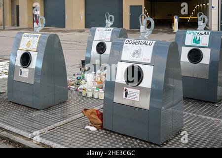 Quattro moderni contenitori in alluminio per materiali riciclabili di fronte all'ingresso di un parcheggio sotterraneo. Le bottiglie sono poste vicino ai contenitori. Foto Stock