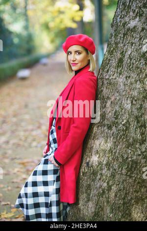 Bella donna di mezza età appoggiata su un tronco d'albero in un affascinante parco urbano. Foto Stock