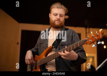 Un ragazzo giovane con una barba suona una chitarra basso con cinque corde Foto Stock