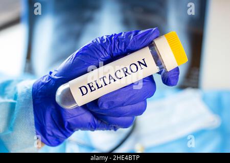 Nuova variante infettiva Deltacron del campione di coronavirus Disease (Delta e Omicron) in provetta da laboratorio nella mano dello scienziato in guanto medico blu su Light ba Foto Stock