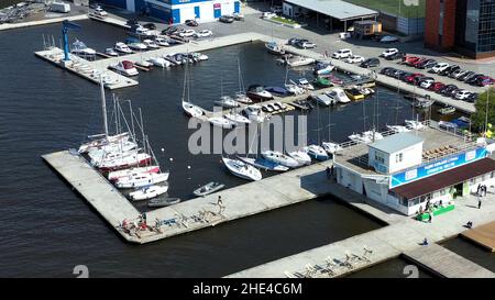 Vista aerea di molti yacht bianchi e motoscafi al porto. Barche a vela ormeggiate al porto in un laghetto della città vicino al parcheggio in una giornata estiva di sole. Foto Stock