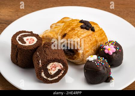 Vista ad angolo di vari dessert in ceramica bianca. Dessert assortito, rotolo di torta in spugna Foresta Nera, pasticceria danese ripiena di crema al cioccolato Foto Stock