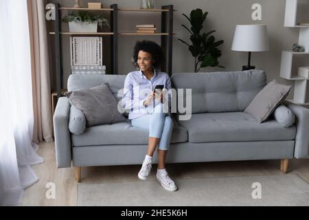 Giovane donna africana sognante che tiene lo smartphone nelle mani. Foto Stock