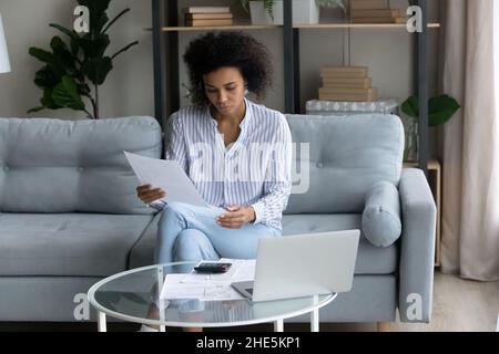 Donna africana focalizzata sul millenario che calcola i conti a casa. Foto Stock