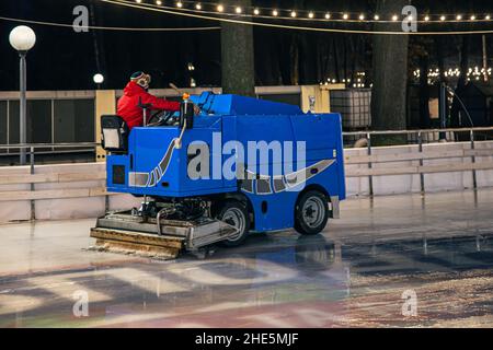 Un operatore dello stadio pulisce una pista di pattinaggio su una moderna macchina per la pulizia del ghiaccio blu. Foto Stock