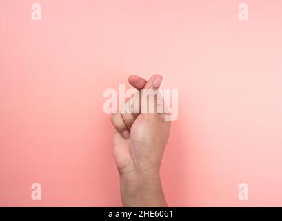 Concetto di amore e cura. Mano che fa un piccolo cuore isolato su uno sfondo rosa. Mini cuore simbolo del linguaggio del corpo gesto fatto da pollice e dito. Foto Stock