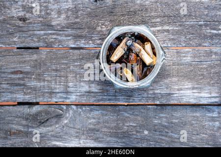 Vista dall'alto di molti mozziconi di sigaretta affumicati in una bottiglia su un tavolo di legno Foto Stock