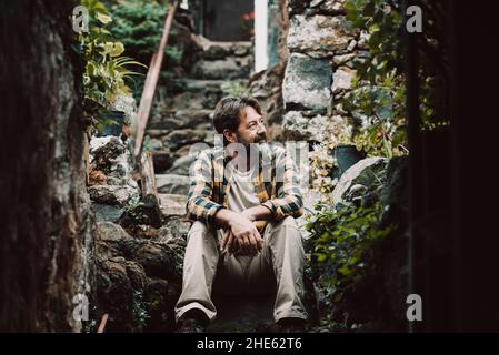 Hipster all'aperto maturo barbuto uomo seduto su una scala rocciosa e godendo la natura intorno osservare e riposare - singolo maschio concetto di stile di vita della gente - r Foto Stock