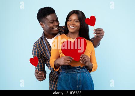 Giovane coppia Romantic Black posa e tenuta di cuori di carta rossa Foto Stock