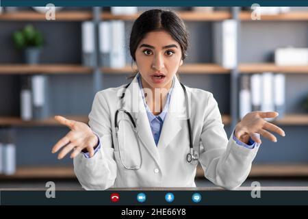 Scioccante eccitato giovane dottore indù in uniforme, con bocca aperta gesturing in ufficio interno sullo schermo del gadget Foto Stock