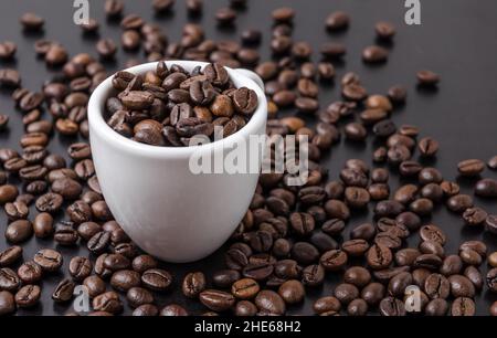 Tazza bianca riempita con chicchi di caffè su sfondo scuro, caffè o concetto barista Foto Stock