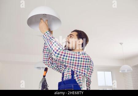 Giovane elettricista in piedi sulla scala e lampada a LED cambiante nella lampada da soffitto Foto Stock