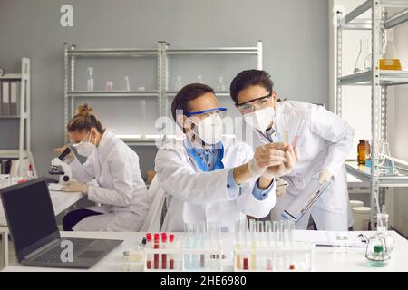 Scienziati che lavorano in laboratorio guardando le provette di vetro e discutendo il loro esperimento Foto Stock