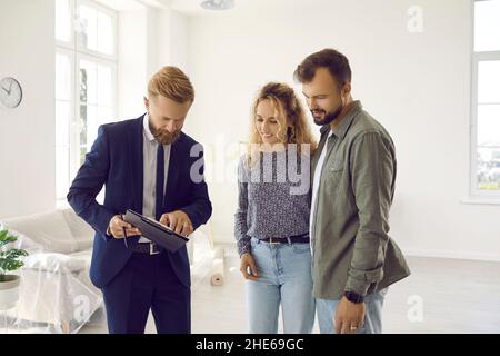Giovane coppia sposata eccitato che va firmare affare con agente di bene immobile durante l'ispezione domestica. Foto Stock