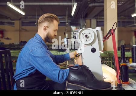 Operatore di fabbrica di scarpe che utilizza una macchina da cucire industriale per realizzare nuovi stivali in pelle nera Foto Stock