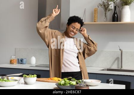 Felice eccitata donna che balla al tavolo da cucina con insalata Foto Stock