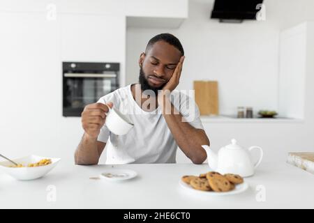 L'uomo nero sbadigia, versando il caffè lontano dalla tazza Foto Stock