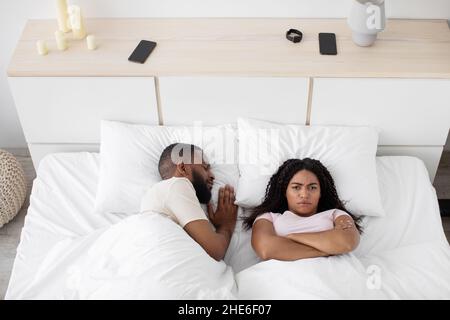 Giovane donna nera sconvolto giaceva sul letto bianco con le braccia incrociate sul petto pensare a problemi, soffre di rumore Foto Stock