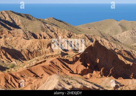 Uomo che si arrampica collina nel canyon fiabesco di Skazka. Lago Issyk-Kul sullo sfondo. Tosor, Kirghizistan Foto Stock