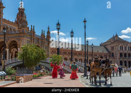 Le Signore in tradizionali costumi di flamenco ballano alla Plaza de Espana, mentre la loro carrozza trainata da cavalli attende per portarle alla Feria de Abril annuale. Foto Stock