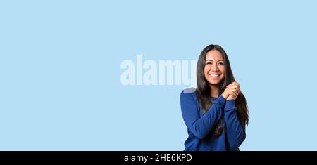 Felice giovane donna con un bel sorriso e mani afferrate che posano su uno sfondo blu con copyspace Foto Stock