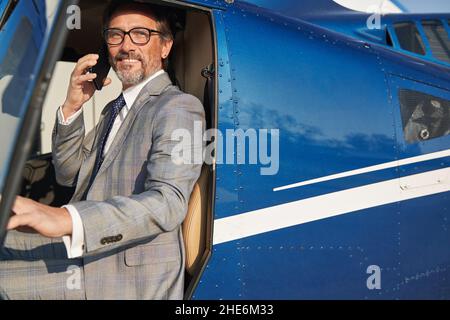 Uomo contento negli occhiali che chiama su smartphone in chopper Foto Stock