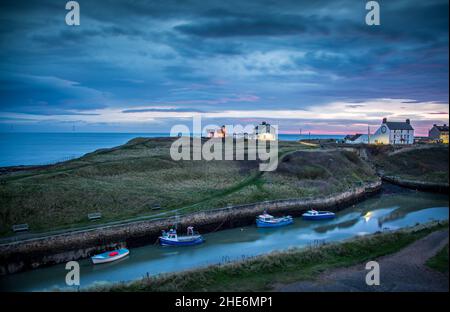 Il Burn con le barche da pesca ormeggiate di Seaton Sluice, Northumberland all'alba, con il cielo ardente che si riflette nell'acqua Foto Stock