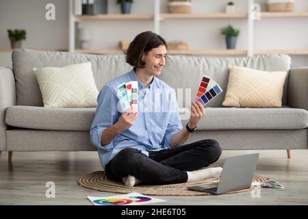 Happy freelance graphic designer ragazzo che lavora con computer portatile e campioni di colore, seduto su tappeto a casa Foto Stock