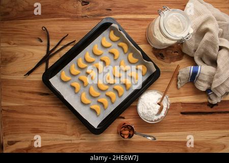 Biscotti non cotti forma a mezzaluna su foglio da forno, vista dall'alto su tavola di legno, preparazione della cottura Foto Stock