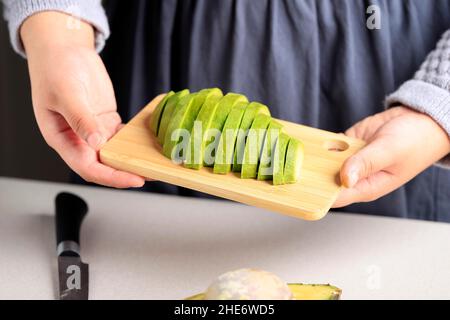 Avocado a fette con coltello su piatto di legno, una donna tenere piatto di legno con avocado a fette Foto Stock