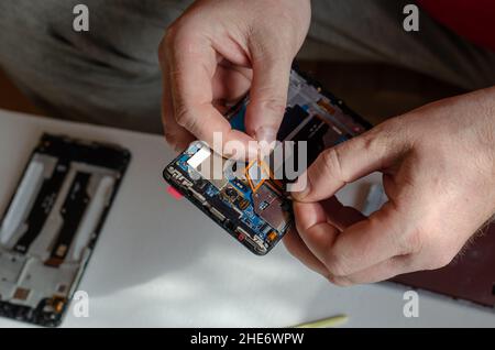 Repair of smartphones concept. A man uninstalls a fingerprint sensor from the board. Part of a series. Indoors. Selective focus. Foto Stock