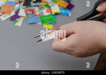 Primo piano delle mani delle donne che distruggono le carte bancarie. Una donna adulta usa le forbici per tagliare le carte di credito da varie banche. Messa a fuoco selettiva. Kiev, Ukrain Foto Stock