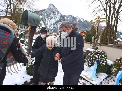 Oberammergau, Germania. 09th Jan 2022. Markus Söder, Ministro-Presidente bavarese (CSU, r), sostiene la vedova di Max Streibl Irmingard Streibl accanto al figlio Florian Streibl dopo una cerimonia di commemorazione del 90th° compleanno dell'ex Ministro-Presidente bavarese Max Streibl presso il cimitero locale. Credit: Karl-Josef Hildenbrand/dpa/Alamy Live News Foto Stock