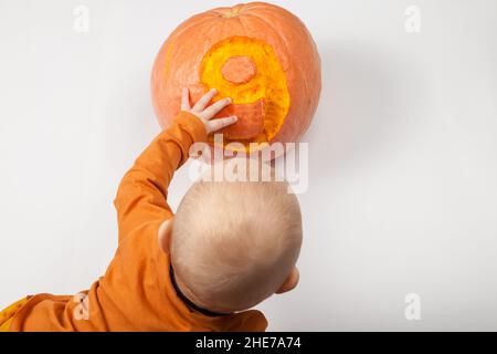 Sorridente neonato felice nove mesi bambino nei vestiti arancioni sul letto luminoso e arioso copia spazio infanzia con zucca con il numero 9 scolpito su di esso Foto Stock