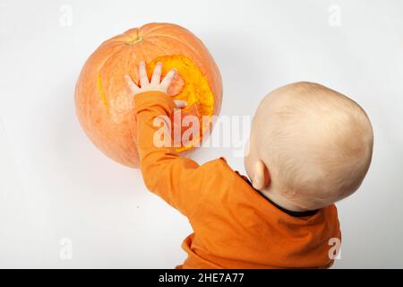 Sorridente neonato felice nove mesi bambino nei vestiti arancioni sul letto luminoso e arioso copia spazio infanzia con zucca con il numero 9 scolpito su di esso Foto Stock